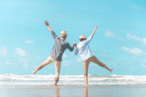 海辺で幸福そうに元気にはしゃぐ老夫婦の写真