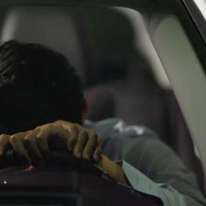 asian businessman feel depressed in car and he is lying on steering wheel at night